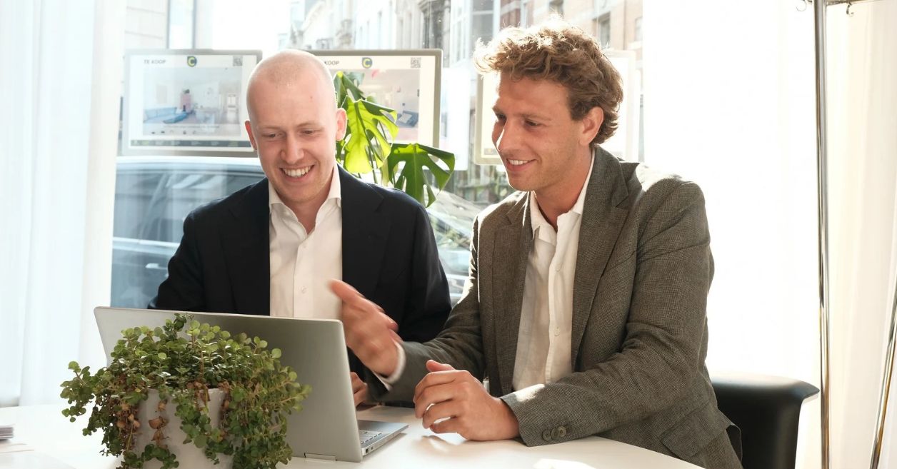 Twee makelaars van Coprimmo bespreken samen een vastgoedproject op een laptop.